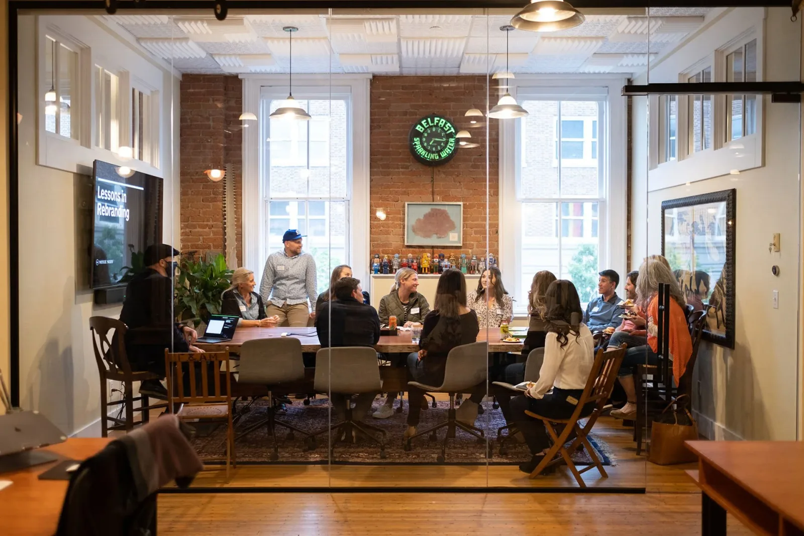 Forum members seated around a long table in a Boulder studio, watching a presentation titled "Lessons in Rebranding".